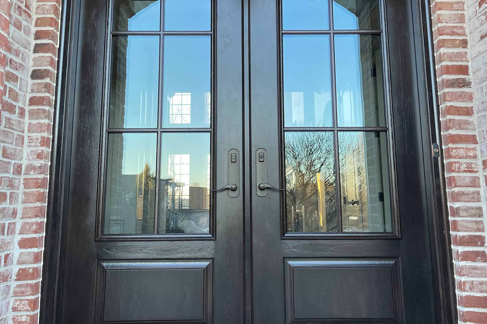 Pair of dark wood-grain entry doors with divided glass panels set into a red brick facade