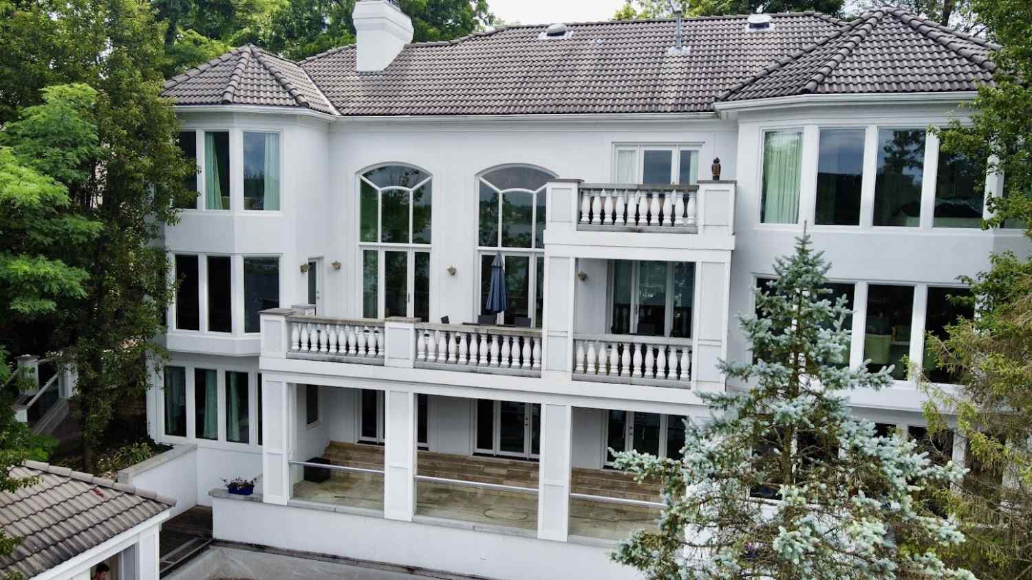 Rear elevation of a large white home with balustraded balconies and a covered lower terrace