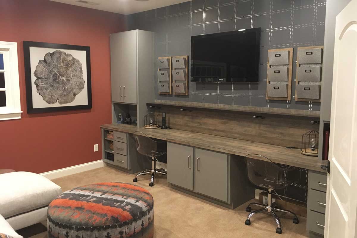 Finished basement with a built-in desk run, grey cabinetry, patterned accent wall and mounted television
