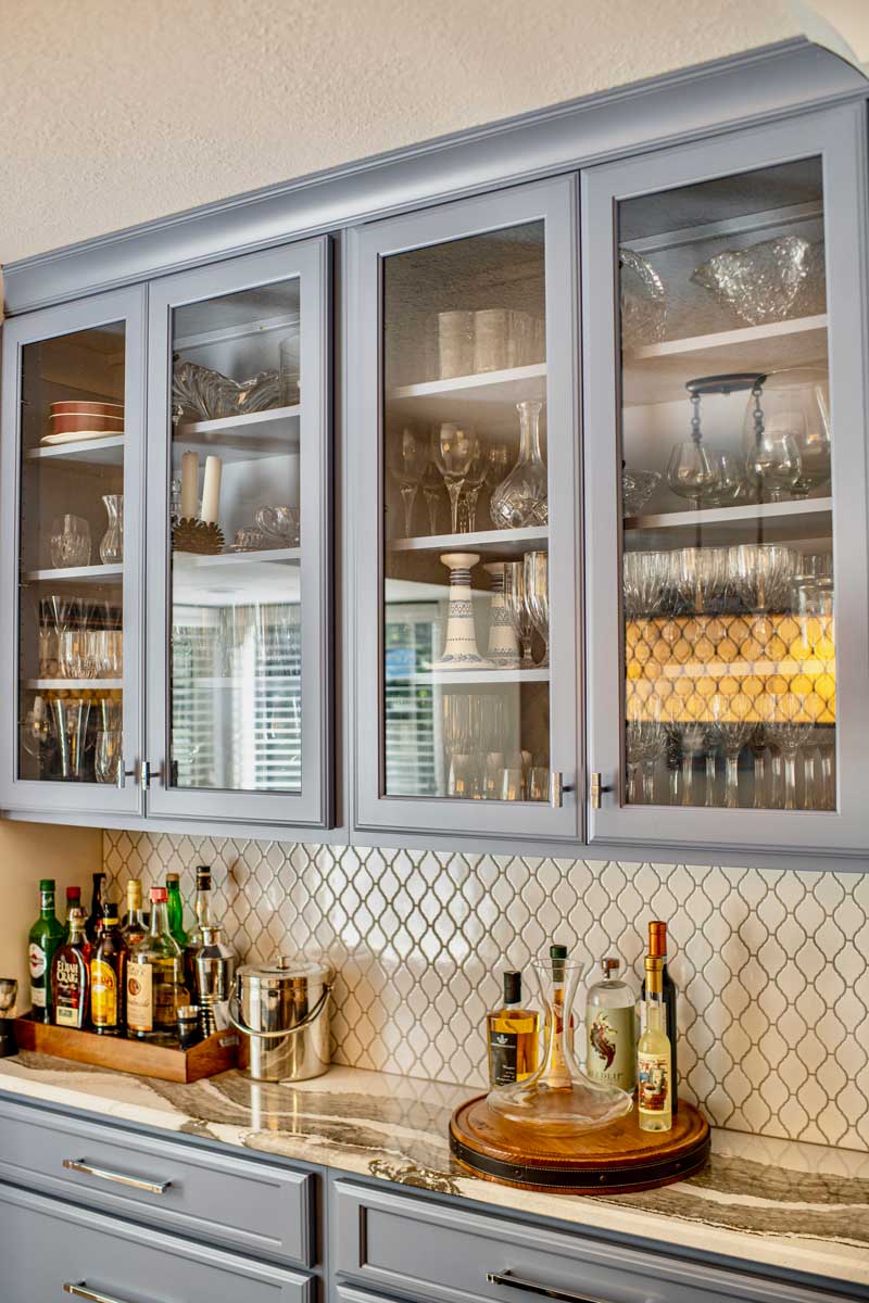 Custom wet bar with glass-front upper cabinets and an arabesque tile backsplash